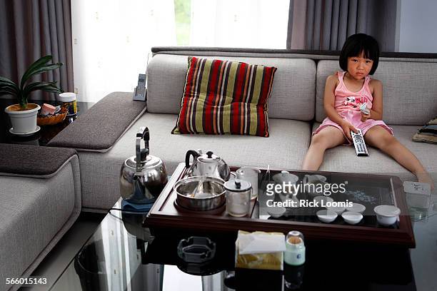 Toying with a remote to a large, flatscreen television, Zhang Yujia sits alone on a large wraparound couch watching cartoons in the nicely...