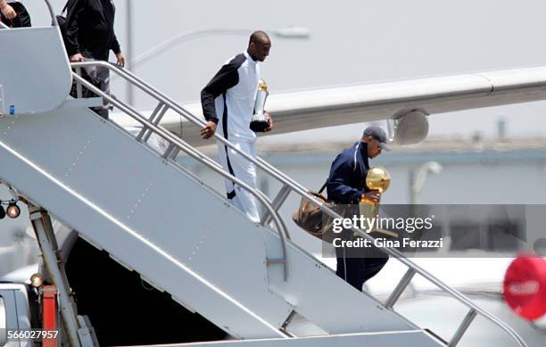 Lakers Kobe Bryant carries his MVP trophy as teammate Derek Fisher carries the championship trophy upon arriving at LAX the morning after beating...