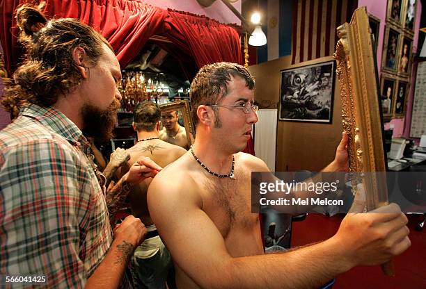 Will Roberts, right, from Stillwater Oklahoma, uses a mirror to check out a tattoo design of tribal art, located on his back, while confering with...