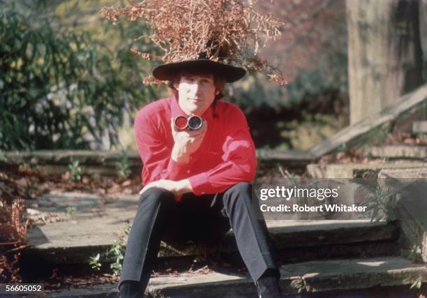 Beatles singer, songwriter and guitarist John Lennon in the garden at his home, 1964. He is wearing a hat adorned with dead fern fronds.