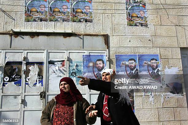 Campaign posters for Palestinian legislative elections are seen on a wall behind Palestinian women watching the funeral of Thabet Ayadi in the West...