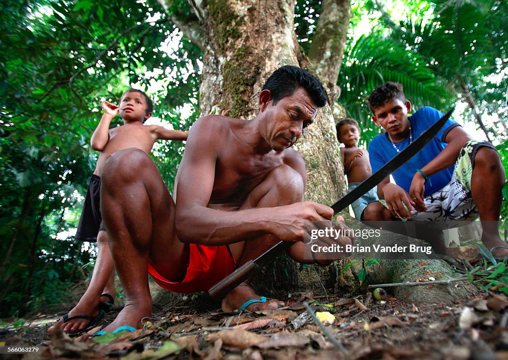 Children watch as Raimundo Nonato shells Brazil nuts with a machete in the Brazilian Amazon communi