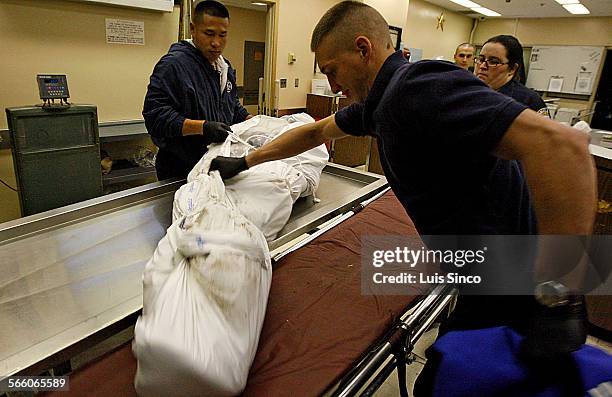 Marine Corps Reserve Sgt. Robert Lee, left, and Cpl. Robert Norton assist Forensic Attendant Wendy Withers with a corpse that was delivered to the...