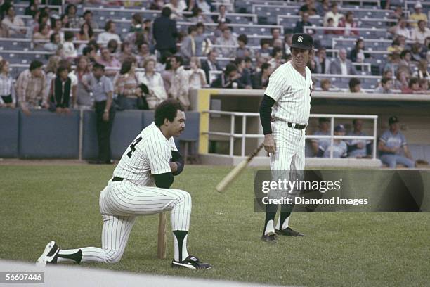 Outfielder Reggie Jackson, of the New York Yankees, takes a knee as manager Billy Martin swings a bat prior to a game against the Kansas City Royals...