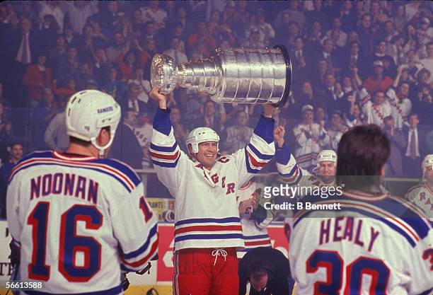 Canadian professional hockey player Mark Messier of the New York Rangers hoists the Stanley Cup championship award trophy over his head as teammates...