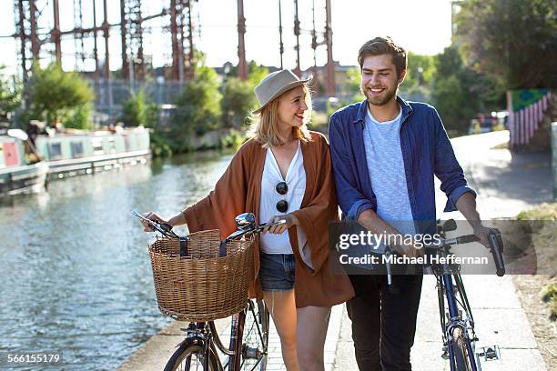 couple smiling and walking along canal with bikes - walking with bike stockfoto's en -beelden