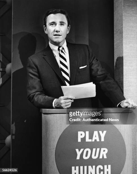 American singer, actor, talk show host, and empresario Merv Griffin holds cards in his hand and leans on the podium as he hosts the premiere episode...