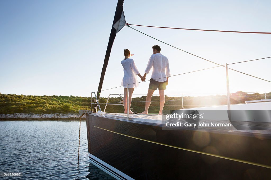 Young couple watching sunrise from bow of yacht.