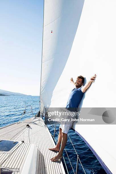 man leans on sail at bow of yacht - voile bateau photos et images de collection