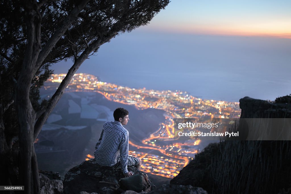 Man sitting on high rock above city at nigt