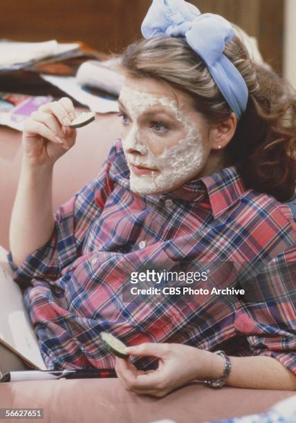 American actress Jane Curtin wears a facial mask as she sits on a couch and holds cucumber slices in a still from the CBS television sitcom 'Kate &...