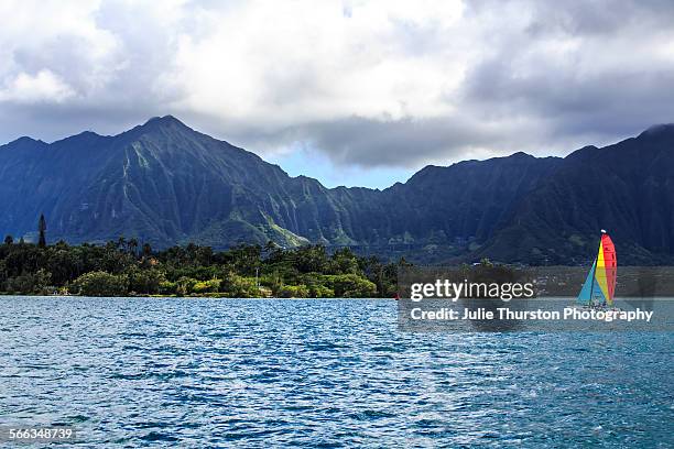 Colorful sailboat with wind blowing through the sails, floats in the waters of Kaneohe Bay with the beautiful Ko'olau Mountain Range and lush...