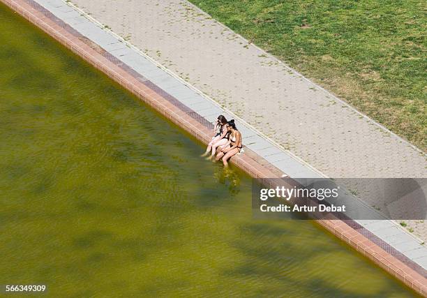 Couple of girls in bikini sitting on the pool edge on summer time cooling off.