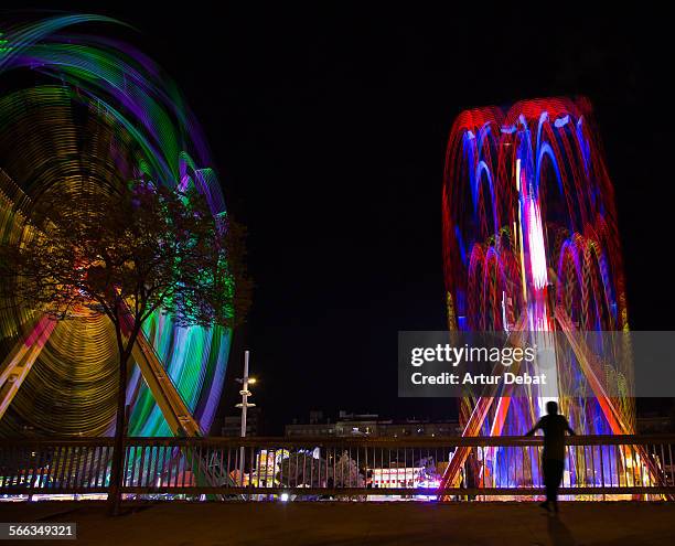 Long exposure view of a two ferris wheel in a fun fair with people on summer night.