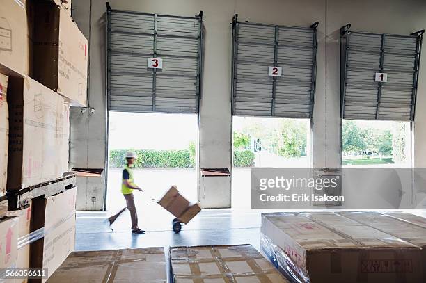 caucasian worker wheeling cardboard boxes in warehouse - helmet cart stock pictures, royalty-free photos & images