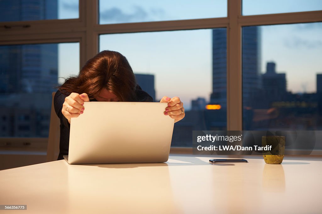 Stressed Caucasian businesswoman holding laptop in office