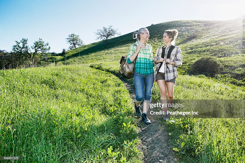 Caucasian mother and daughter walking on grassy hillside