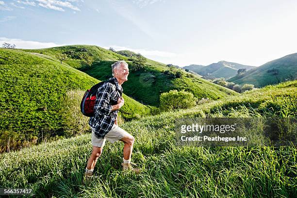 older caucasian man walking on grassy hillside - walking side view stock-fotos und bilder