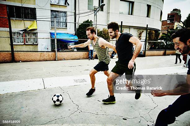 soccer players converging on ball in urban park - soccer men stock-fotos und bilder