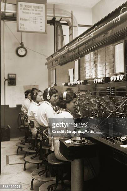 Women operators making connections at a 1920s telephone switchboard; toned photograph, circa 1920.