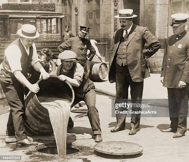 Policemen in New York City pour liquor from a barrel down a sewer, in a raid during Prohibition; photograph, 1921.