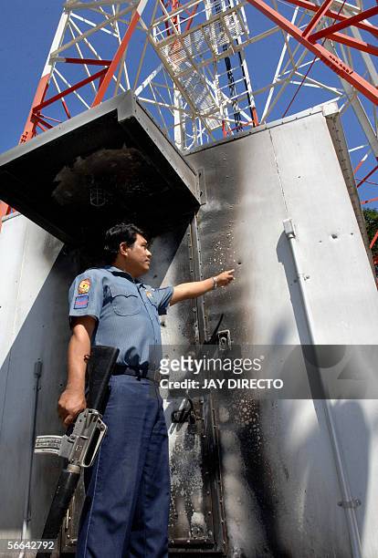 An unidentified police officer armed with an assault rifle points 11 January 2006 to bullet holes that tore through the partly burned metal enclosure...