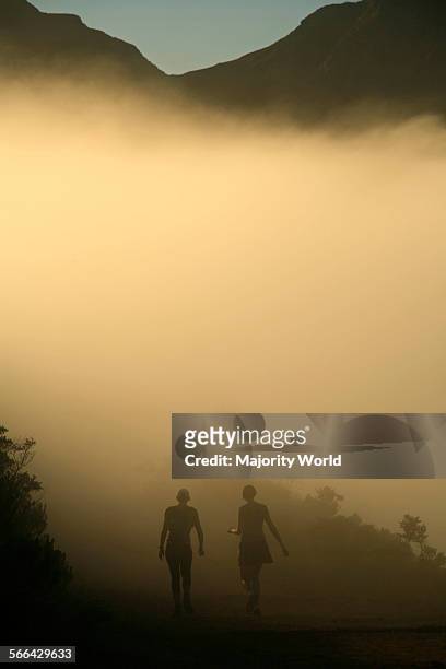 Runners walk down Lions Head into the mist with Table Mountain in the background, Cape Town, South Africa.