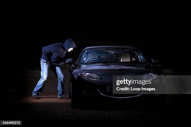Man breaking into a parked car at night.