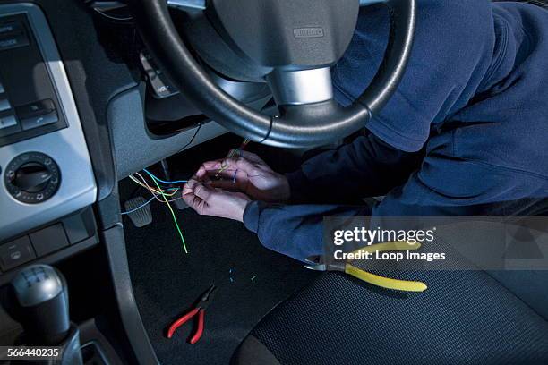 Man wearing a hoody hot wiring a car.