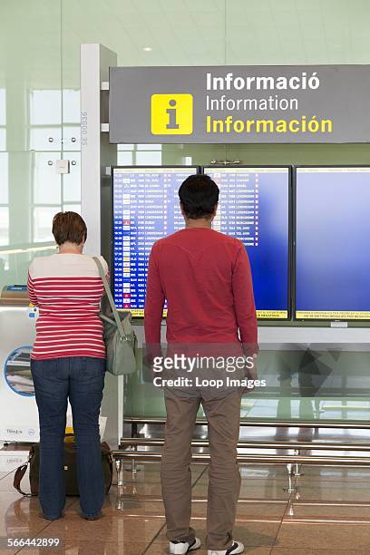 Passengers reading the departures information board at Barcelona Airport.