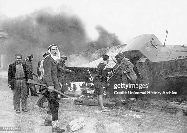 Photograph of Arab irregulars, along with a burnt truck on the way to Jerusalem during the war of Independence. Dated 1948.