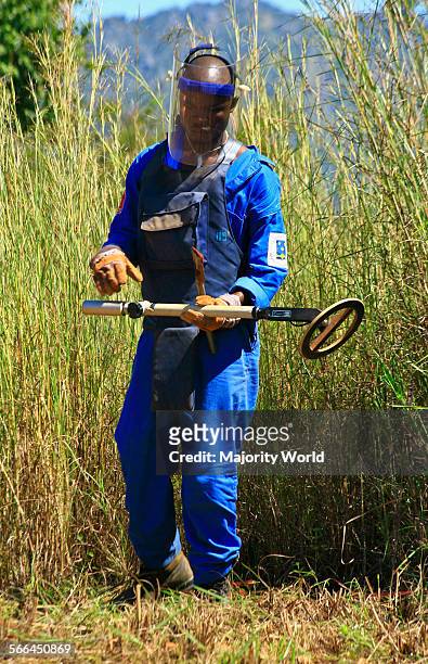 Man wearing a protective face mask holds a metal detector used in demining operations to remove the land mines planted in Angola during the civil...