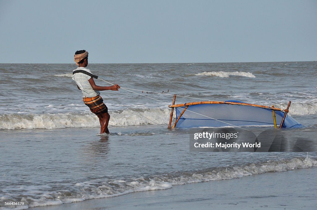 A young man catches shrimp with a net from the Bay of Bengal