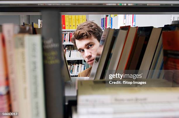 a man peering through a bookshelf - spähen stock-fotos und bilder
