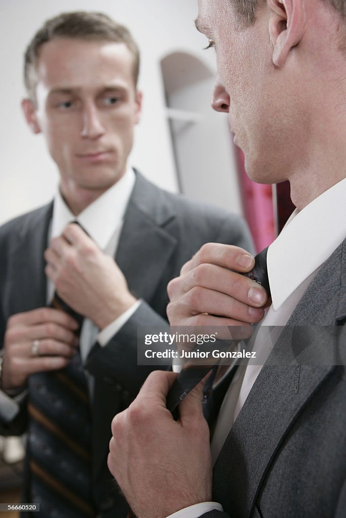 A man straightening his tie in a mirror