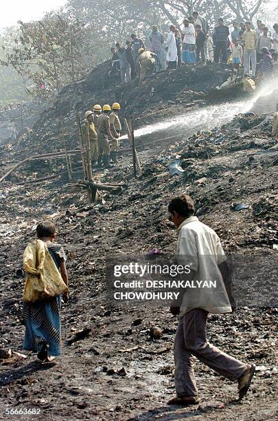 Two Indian slum dweller search for their remaining belongings at a fire devasted site while fire fighters spray water to control the remaining embers...