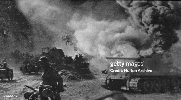 Soviet soldiers walk and drive past a burning T-34 medium tank during the Battle of Kursk, Russia, July 1943. Although the conflict between the...