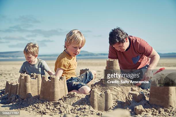 father and sons playing on the beach - zandkasteel stockfoto's en -beelden