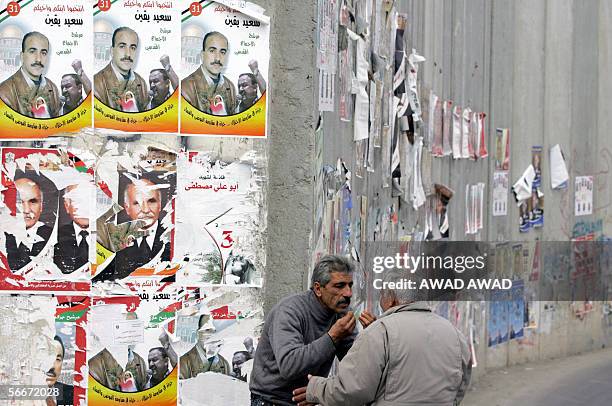 Palestinian men discuss the issues of the day as they stand close to the Israeli built "separation barrier" plastered with Palestinian election...