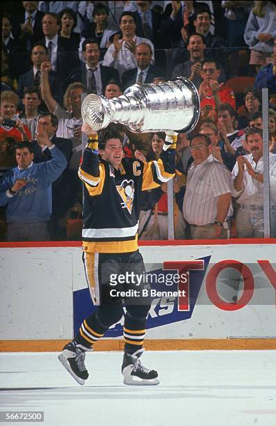Canadian professional hockey player Mario Lemieux, forward for the Pittsburgh Penguins, hoists the Stanley Cup over his head and takes it for a...