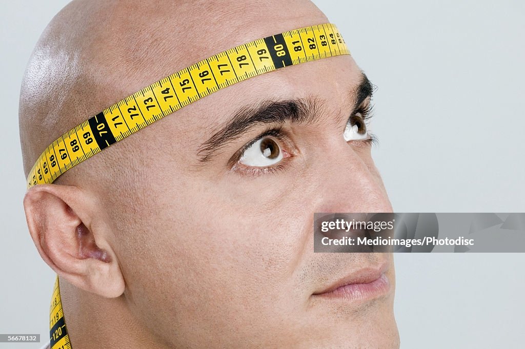 Mid adult man with a measuring tape around his head