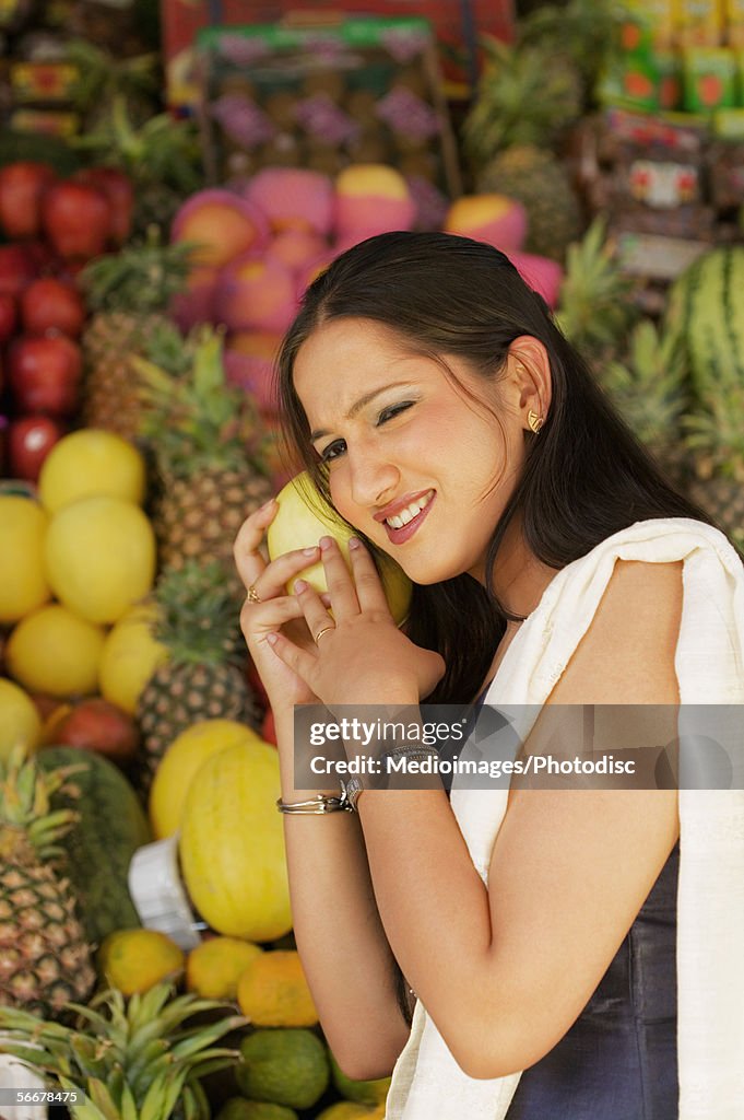Young woman holding a mango up to her ear