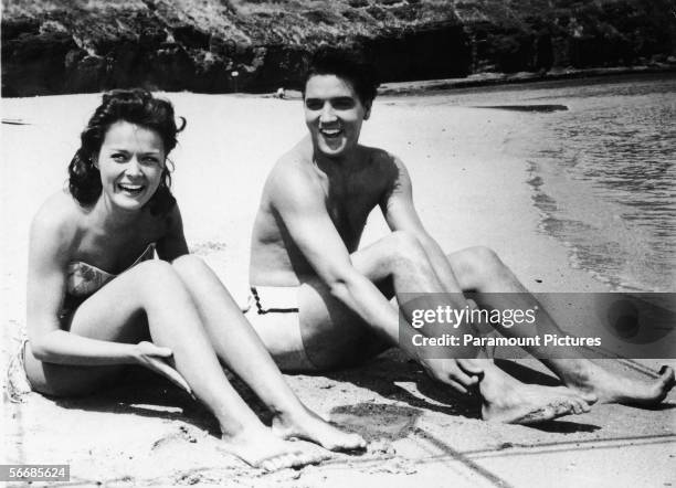 American singer and actor Elvis Aron Presley and American actress Joan Blackman , both dressed in swimsuits, sit on the beach in a still from the...