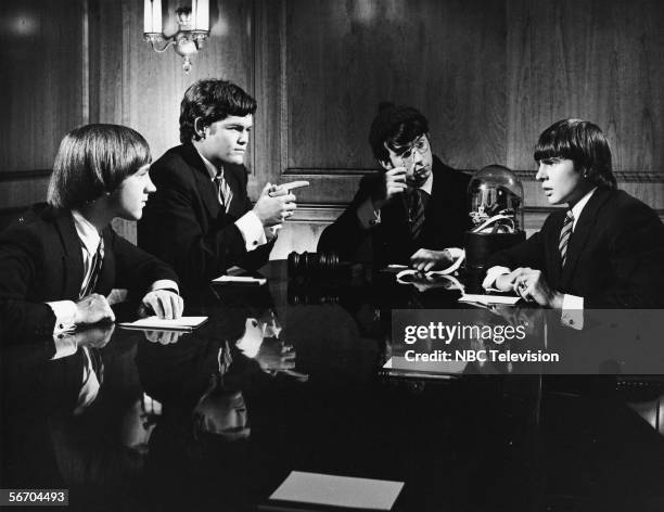 Musician/actors the Monkees, all dressed in suits, sit around a board room table equipped with a stook ticker in a scene from the television show...