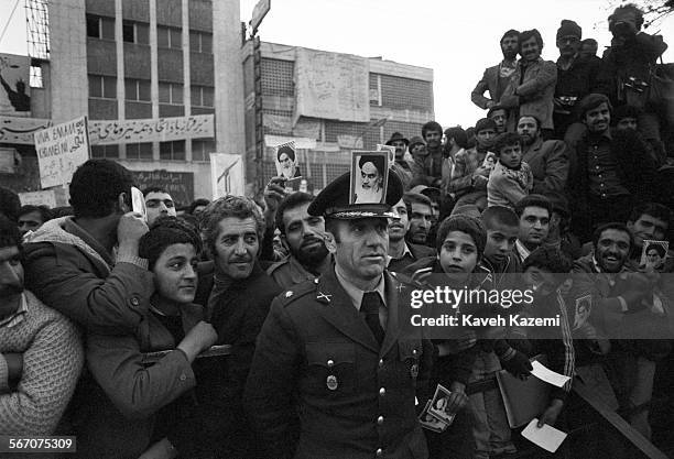 An army officer with a photo of Ayatollah Khomeini on his hat stands among people demonstrating outside the American Embassy which is occupied by...