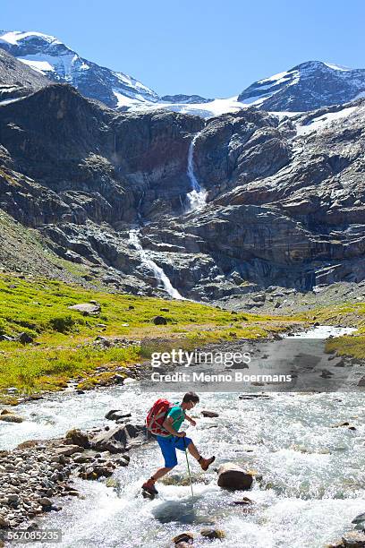 a male hiker jumping from stone to stone to cross a river, during the glocknerrunde, a 7 stage trekking from kaprun to kals around the grossglockner, the highest mountain of austria. - hohe tauern stock pictures, royalty-free photos & images