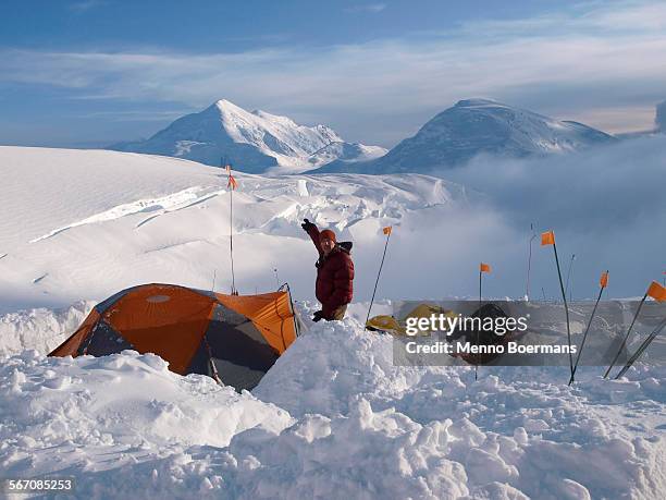 climber and ranger is standing next to his tent and pointing to mount foraker from 12.000 feet camp high on mount mckinley. - フォーレイカー山 ストックフォトと画像