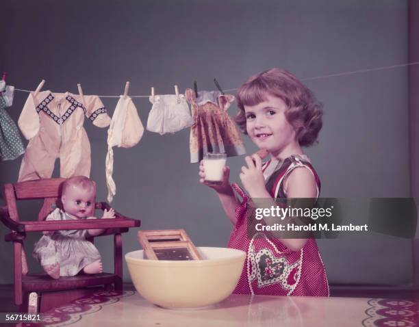 Little girl playing at being mother takes a break for milk and cookies, 1956.