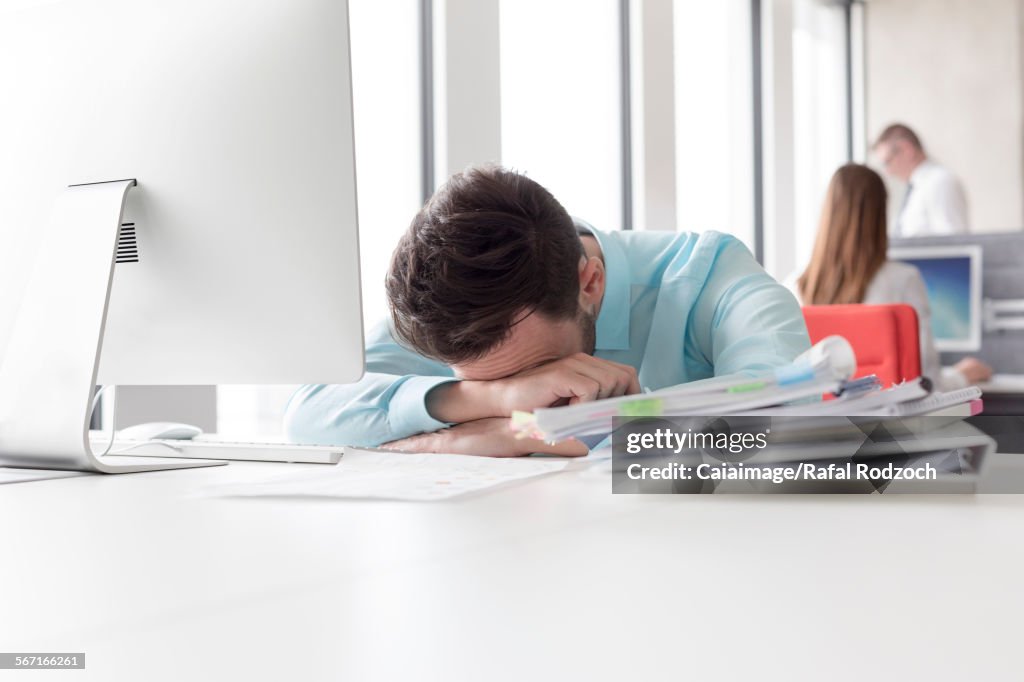 Frustrated businessman with head down next to stack of reports on desk