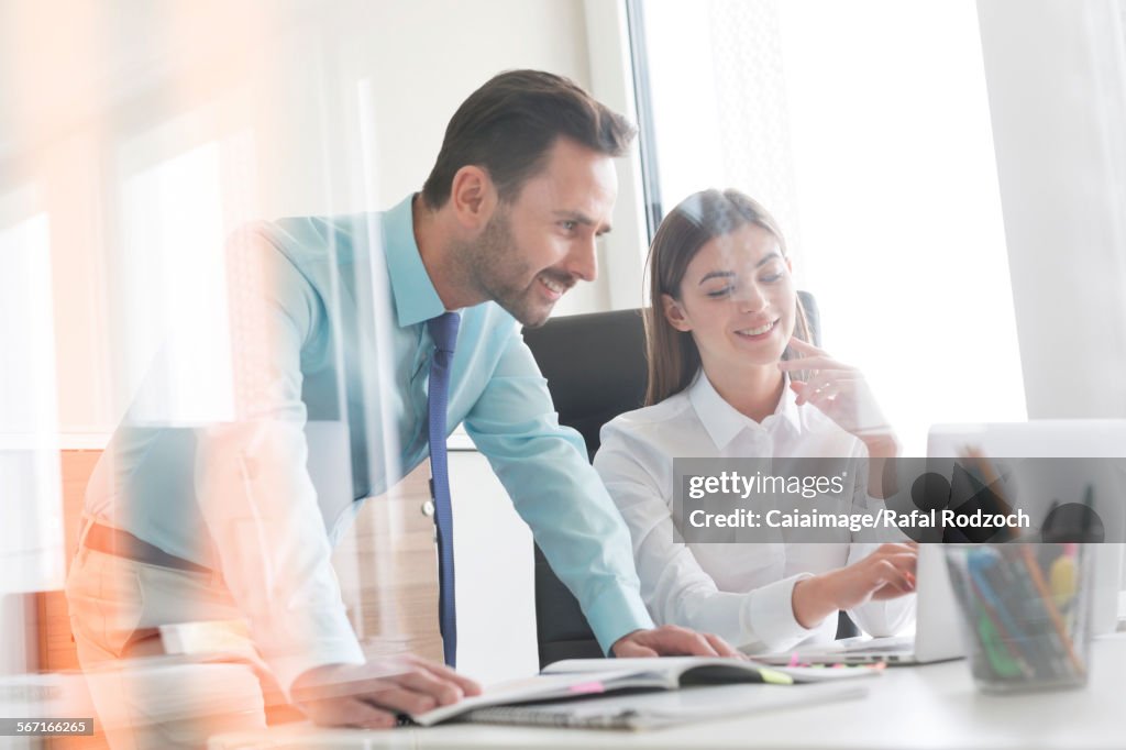 Businessman and businesswoman working at laptop in office